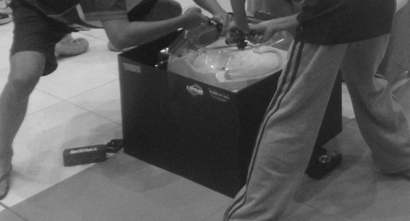 Un giocatore e il suo avversario lanciano con le mani sopra un'arena di Beyblade X posata su una scatola nera